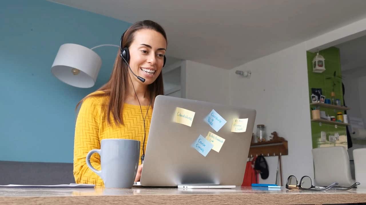 Young woman working at home as a customer service representative wearing a headset while typing on laptop